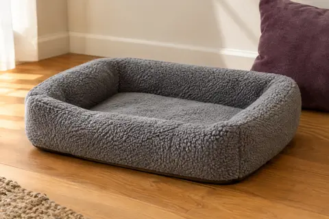 Panier rectangulaire gris pour chat, avec surface en sherpa et rebord rembourré, posé sur un parquet.