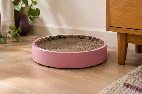 Griffoir circulaire rose en carton ondulé posé au sol dans un intérieur chaleureux et lumineux.