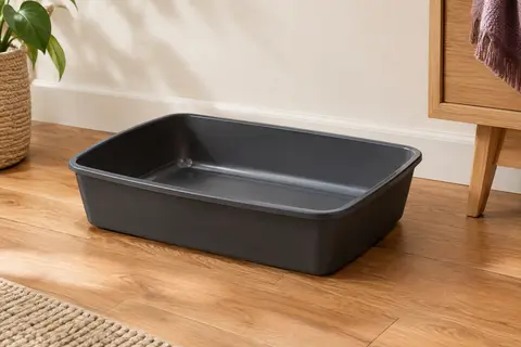 Bac à litière ouvert en plastique anthracite posé sur un sol en bois clair dans un intérieur crème.