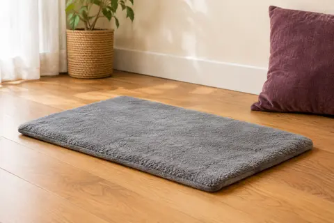 Tapis autochauffant gris en polaire posé sur un parquet dans un intérieur chaleureux